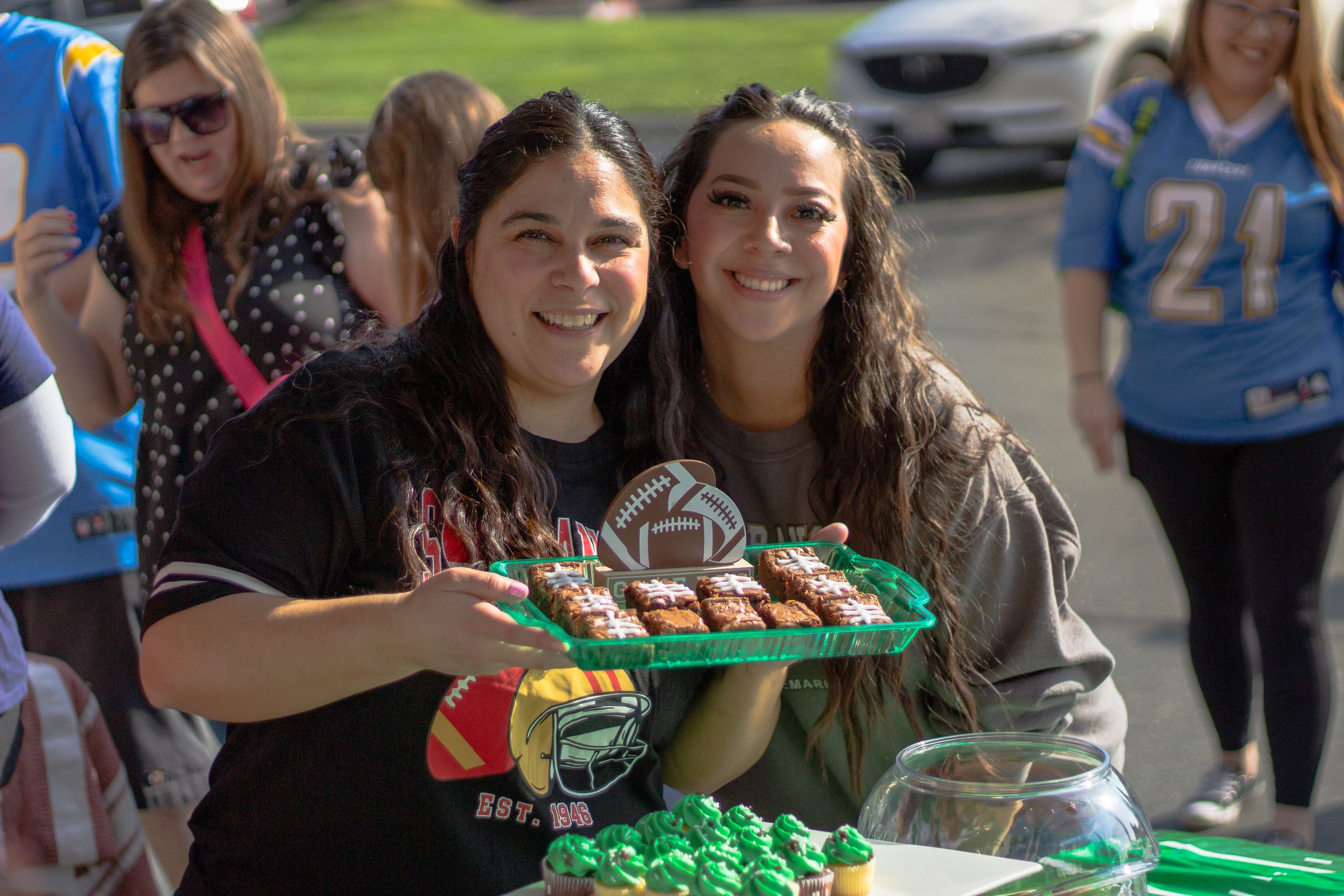 Two women smiling with a tray of football-themed treats at a LifeBridge event